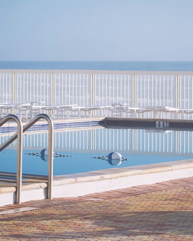 Calm oceanfront pool at morning with white lounge chairs and ocean horizon beyond