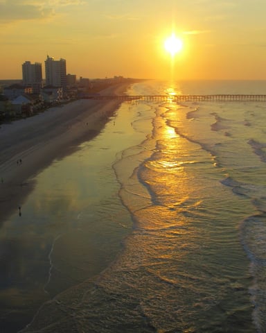 Golden sunset aerial over Myrtle Beach with condos and pier reflecting on wet sand