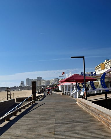 Beach boardwalk with shops, restaurants, and condos stretching along the shoreline under blue sky