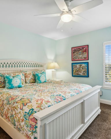 Bright coastal vacation rental bedroom with white wicker furniture, teal accents, and shuttered windows
