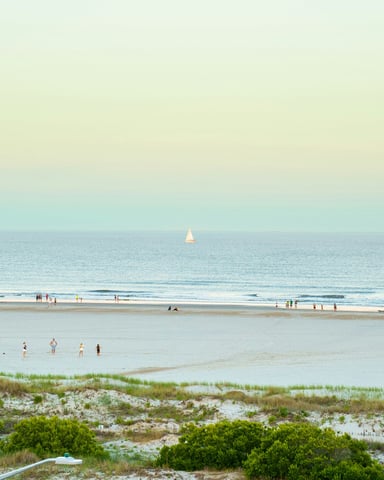 Wide beach at dusk with a sailboat on the horizon and soft pastel sky over the Atlantic
