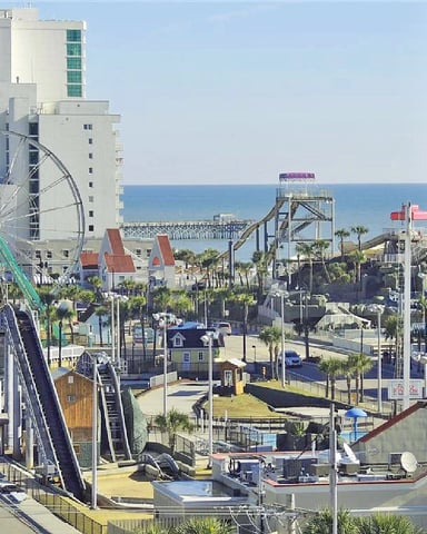 Beachfront amusement park with Ferris wheel, roller coaster, and boardwalk overlooking ocean and pier