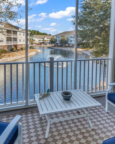Waterfront deck with blue cushioned seating, overlooking pond and residential buildings on sunny day