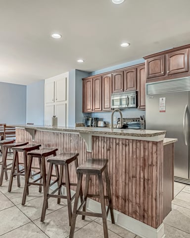 Open-plan kitchen and dining area with wood cabinetry, stainless steel appliances, island with bar seating, and beach-themed artwork