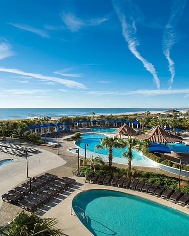 Aerial view of resort with multiple pools, water slides, palm trees, and ocean coastline under blue sky