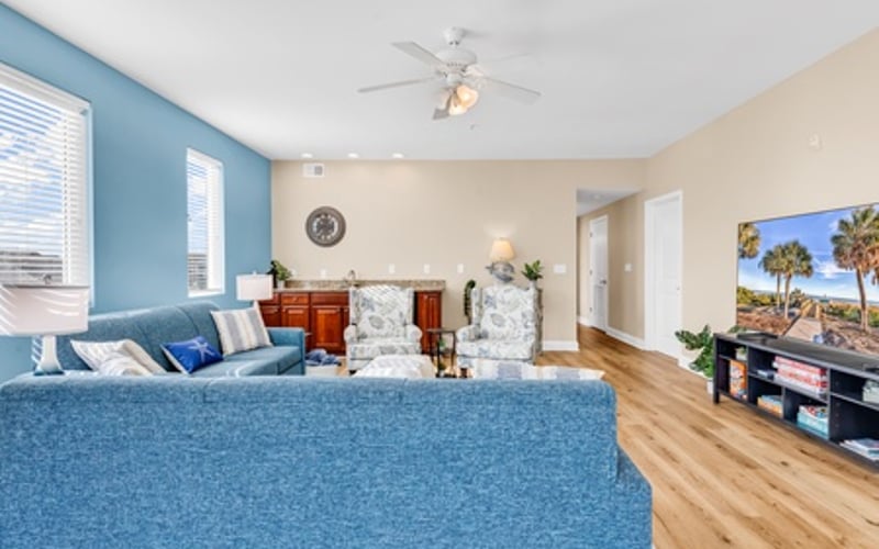 Spacious bedroom with blue accent wall, ceiling fan, hardwood floors, and TV entertainment area