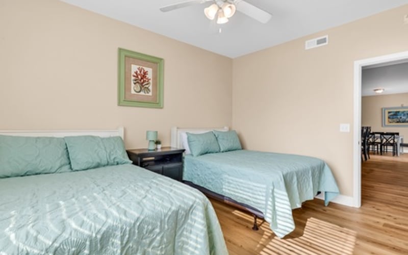Bedroom with two twin beds with light blue bedding, ceiling fan, and doorway to kitchen