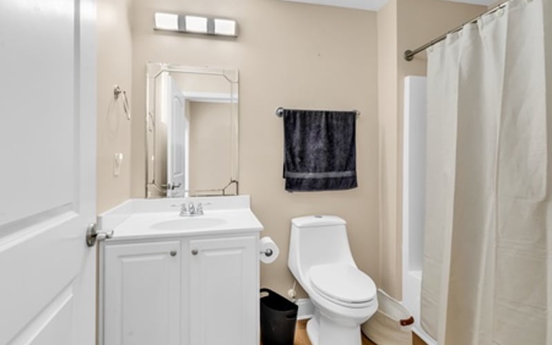 Bathroom with white vanity, toilet, and shower with cream curtain on wood floor