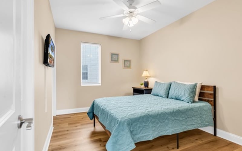 Bedroom with queen bed, blue bedding, ceiling fan, window, and hardwood floors