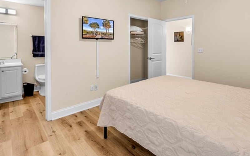 Bedroom with queen bed, wall-mounted TV, wooden flooring, and ensuite bathroom visible through open door